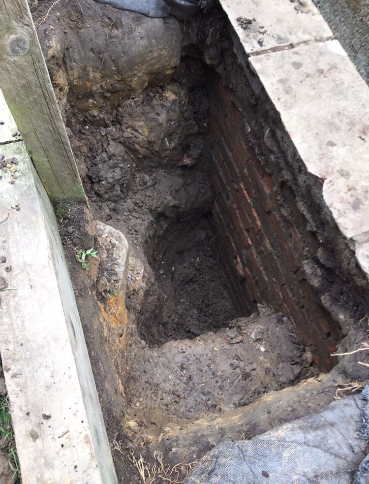 Trial dig exposing an existing retaining wall foundation for inspectio